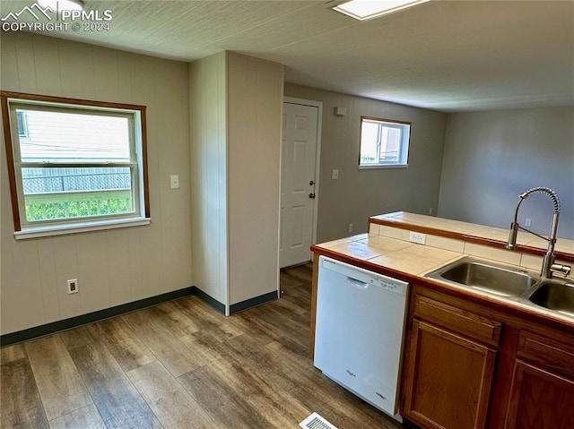 kitchen featuring dishwasher, light hardwood / wood-style floors, tile counters, sink, and a healthy amount of sunlight