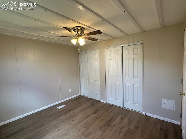 unfurnished bedroom with two closets, ceiling fan, beam ceiling, and dark hardwood / wood-style flooring