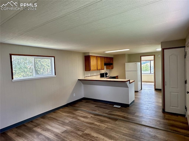 kitchen with dark wood-type flooring, white refrigerator, kitchen peninsula, and sink