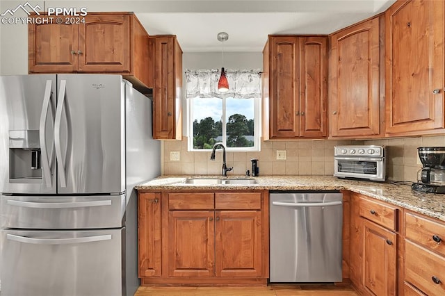 kitchen with backsplash, light wood-type flooring, appliances with stainless steel finishes, light stone counters, and sink