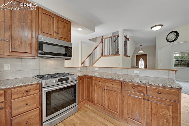 kitchen featuring kitchen peninsula, light stone counters, appliances with stainless steel finishes, and light hardwood / wood-style floors