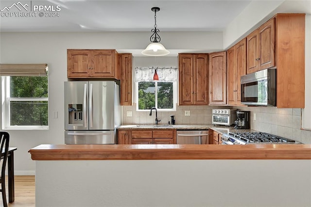 kitchen with stainless steel appliances, light hardwood / wood-style floors, sink, kitchen peninsula, and tasteful backsplash