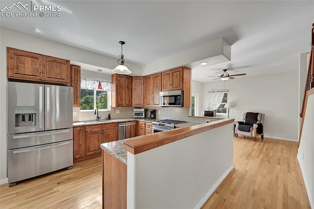 kitchen featuring light wood-type flooring, stainless steel appliances, kitchen peninsula, ceiling fan, and pendant lighting