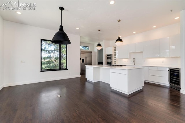 kitchen with white cabinets, decorative light fixtures, appliances with stainless steel finishes, beverage cooler, and a kitchen island