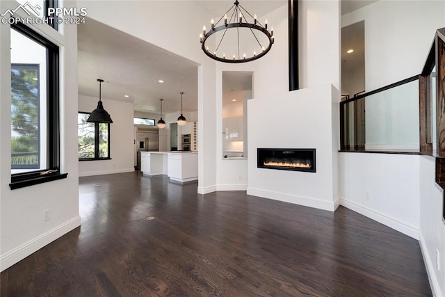 unfurnished living room with dark hardwood / wood-style floors, an inviting chandelier, and a towering ceiling