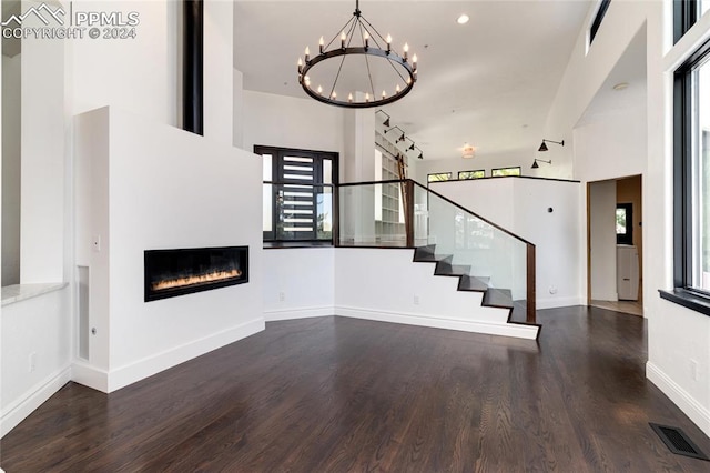 unfurnished living room featuring track lighting, a high ceiling, a notable chandelier, and dark hardwood / wood-style floors