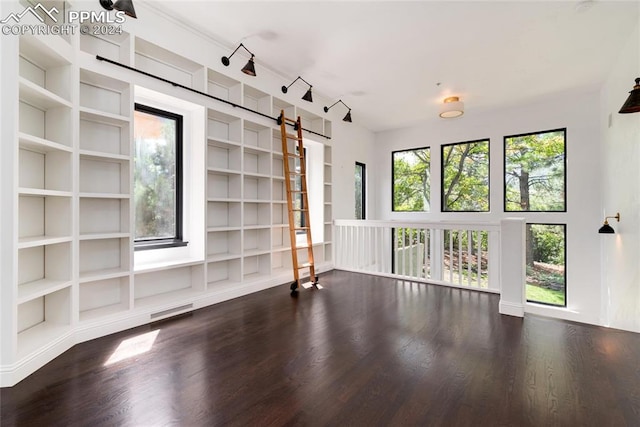 empty room featuring a barn door, rail lighting, dark hardwood / wood-style floors, and built in shelves