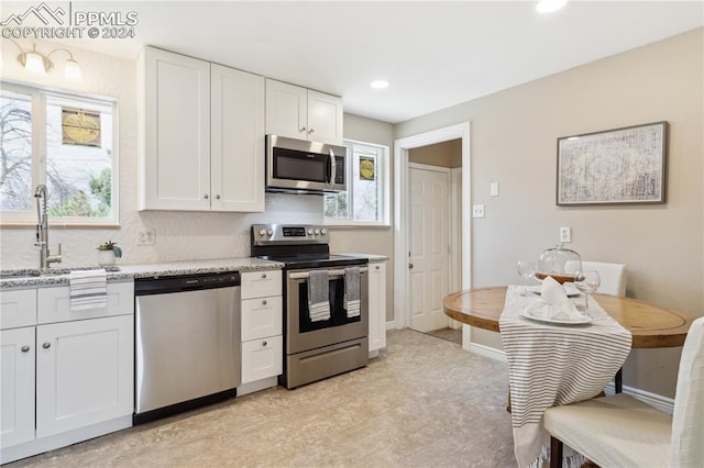 kitchen featuring stainless steel appliances, sink, light stone countertops, and white cabinets