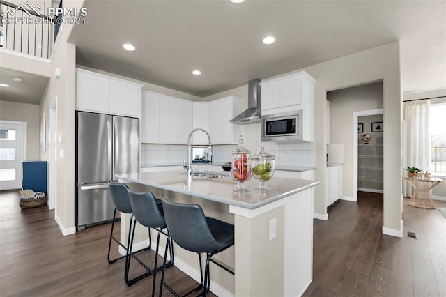 kitchen featuring built in appliances, a center island with sink, dark wood-type flooring, sink, and wall chimney range hood