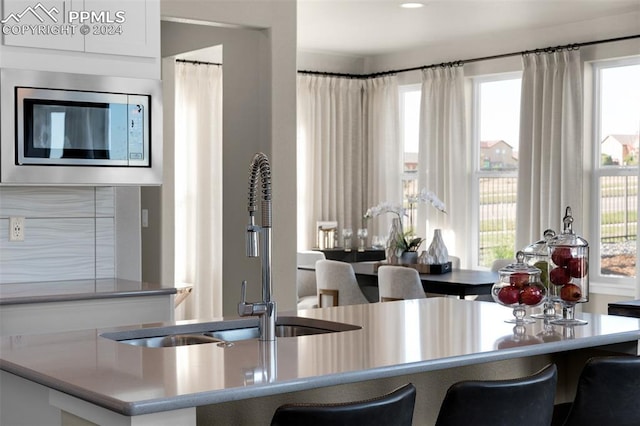 kitchen featuring stainless steel microwave, a healthy amount of sunlight, sink, and a breakfast bar