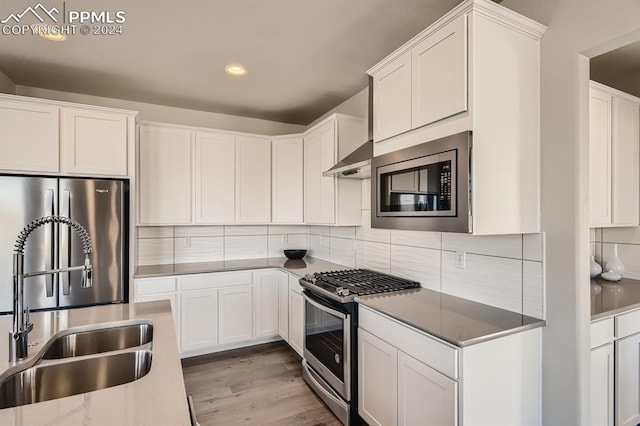 kitchen with light hardwood / wood-style floors, tasteful backsplash, stainless steel appliances, sink, and white cabinets