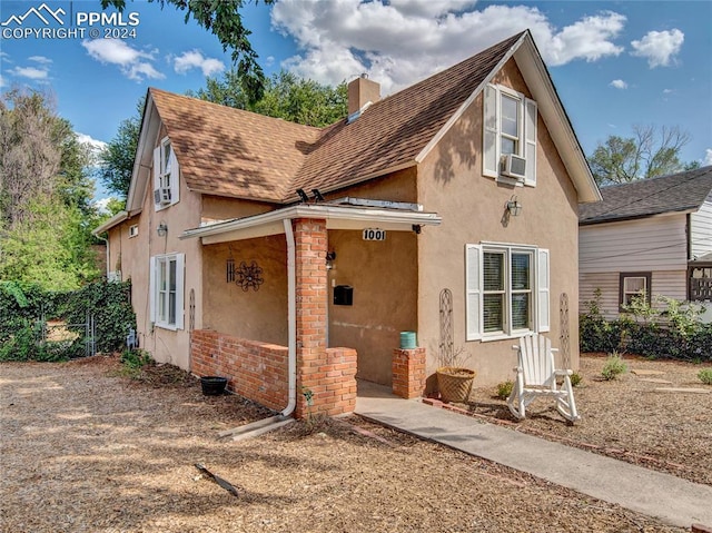 view of front facade featuring roof with shingles, a chimney, cooling unit, and stucco siding