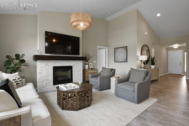 living room with wood-type flooring, a stone fireplace, and high vaulted ceiling