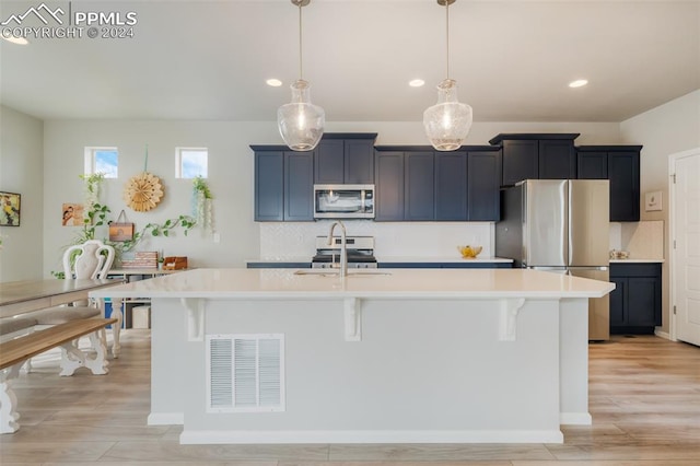 kitchen featuring a center island with sink, hanging light fixtures, appliances with stainless steel finishes, and light hardwood / wood-style floors