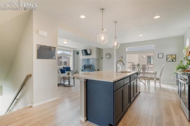 kitchen with light hardwood / wood-style flooring, decorative light fixtures, sink, a center island with sink, and stainless steel gas range oven