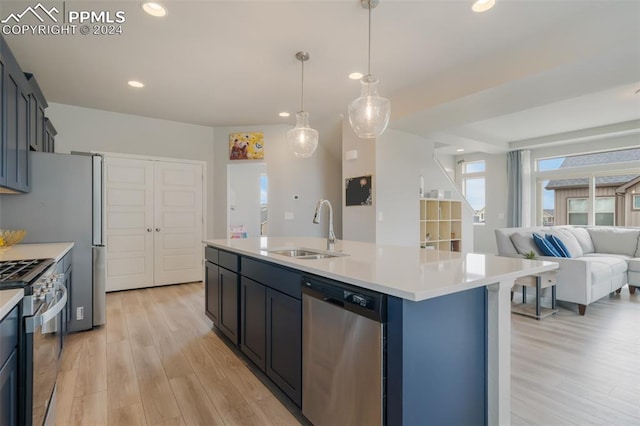 kitchen with pendant lighting, appliances with stainless steel finishes, a kitchen island with sink, sink, and light wood-type flooring