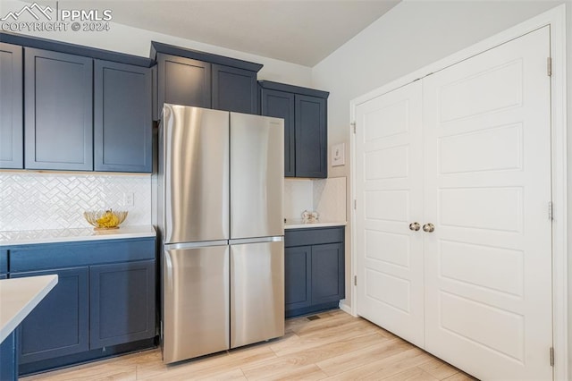 kitchen featuring tasteful backsplash, light hardwood / wood-style floors, stainless steel refrigerator, and blue cabinetry