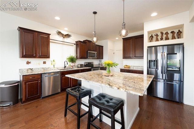 kitchen featuring dark wood-type flooring, a kitchen breakfast bar, decorative light fixtures, a kitchen island, and stainless steel appliances