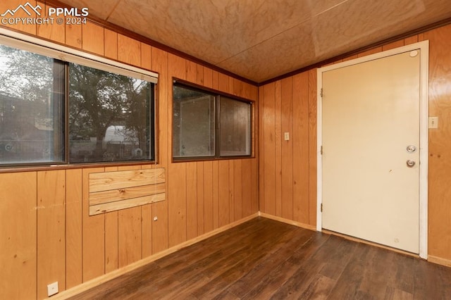 empty room with ornamental molding, dark hardwood / wood-style flooring, and wooden walls