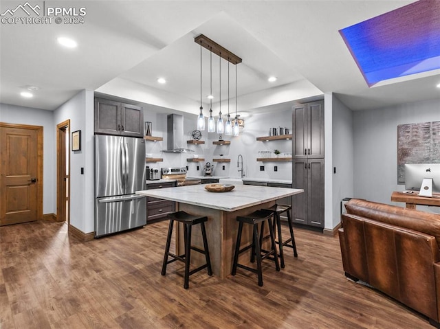 kitchen with a kitchen island, dark hardwood / wood-style floors, appliances with stainless steel finishes, a breakfast bar, and wall chimney range hood