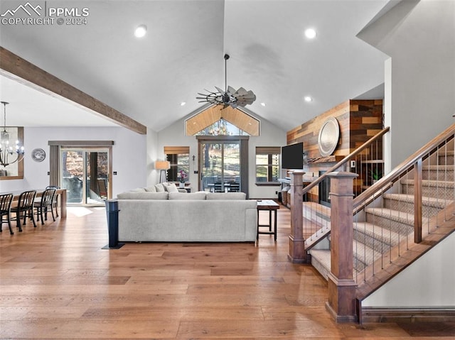 living room featuring ceiling fan with notable chandelier, wood-type flooring, and vaulted ceiling with beams