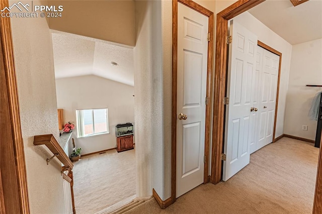 hall with lofted ceiling and light carpet