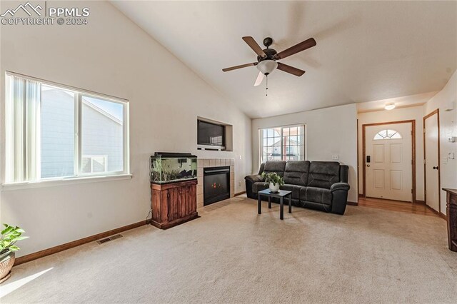 carpeted living room with a tiled fireplace, ceiling fan, and high vaulted ceiling