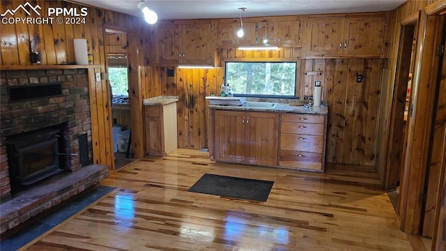 interior space with light wood-type flooring, wood walls, a brick fireplace, and a healthy amount of sunlight