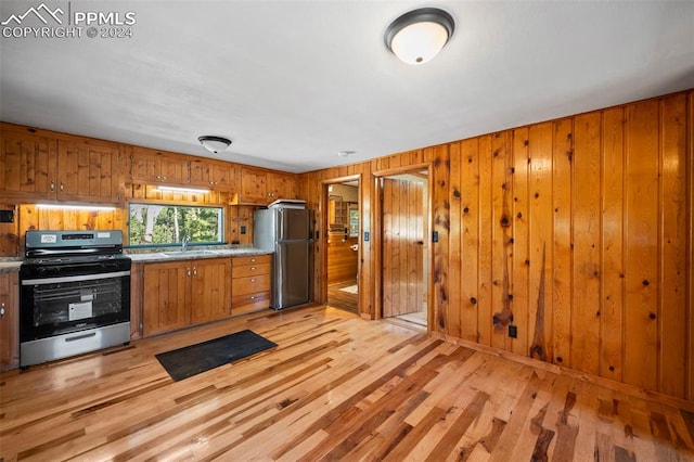 kitchen featuring light wood-type flooring, stainless steel appliances, sink, and wooden walls