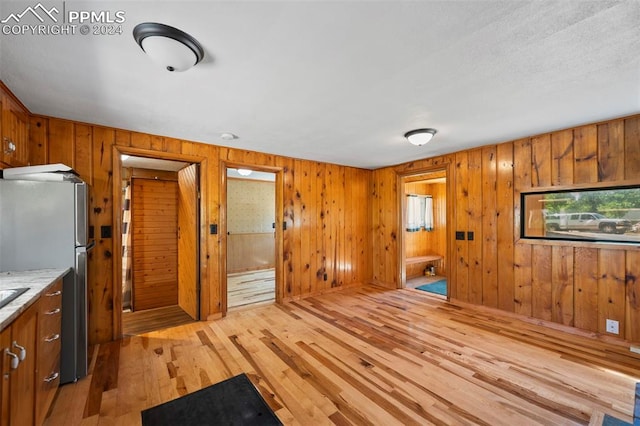 kitchen with stainless steel fridge, wooden walls, and light hardwood / wood-style floors