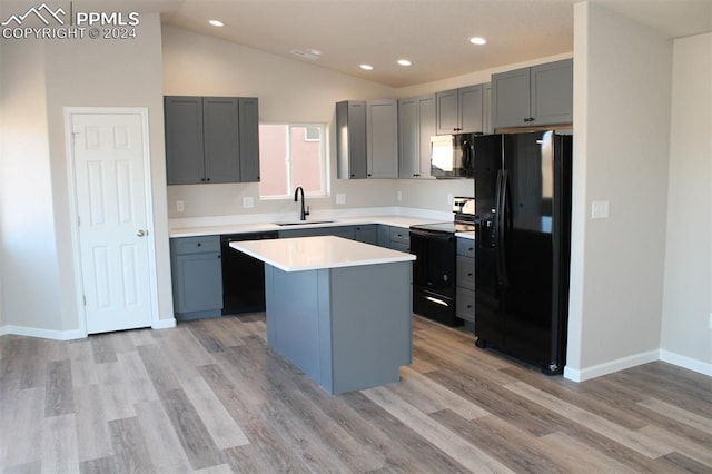 kitchen featuring black appliances, light hardwood / wood-style flooring, a center island, sink, and lofted ceiling