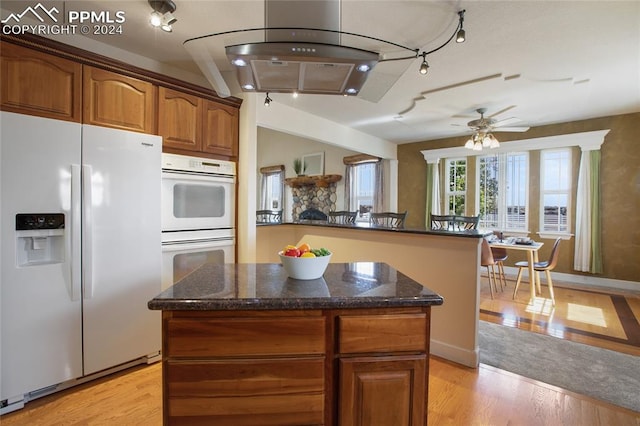 kitchen with ceiling fan, white appliances, light hardwood / wood-style flooring, a center island, and dark stone countertops