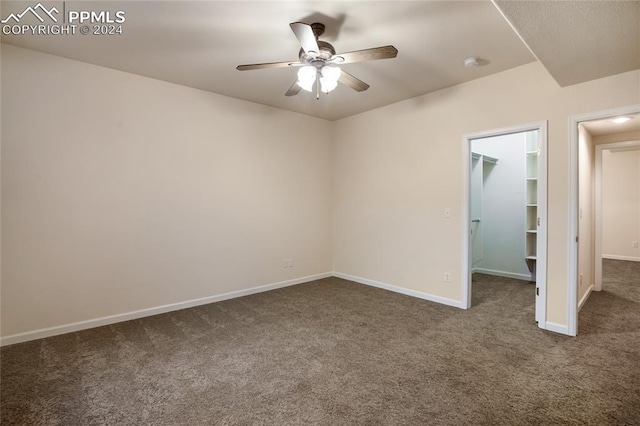 unfurnished bedroom featuring a spacious closet, ceiling fan, dark colored carpet, and a closet