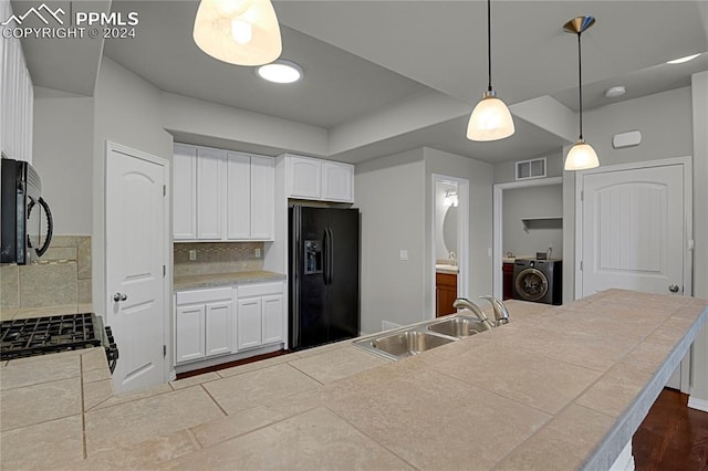 kitchen with decorative light fixtures, black appliances, sink, white cabinets, and washer / clothes dryer