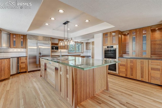 kitchen featuring stainless steel built in fridge, decorative light fixtures, a raised ceiling, and a spacious island