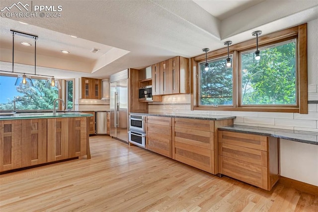 kitchen featuring light wood-type flooring, decorative backsplash, pendant lighting, and stainless steel appliances