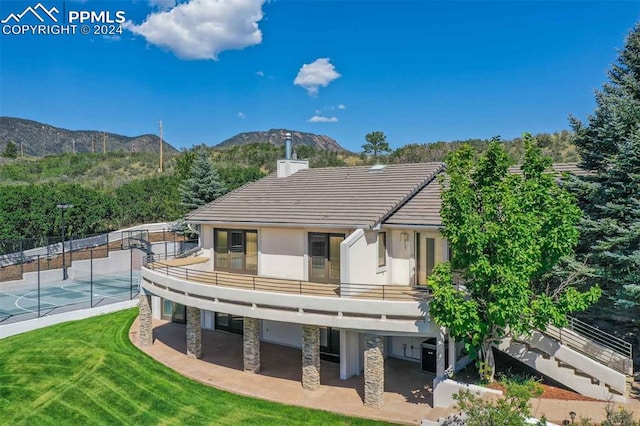 back of house with a mountain view, a balcony, a lawn, and a patio