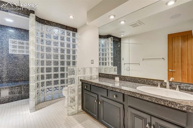 bathroom featuring tile walls, tiled shower, vanity, toilet, and tile patterned floors