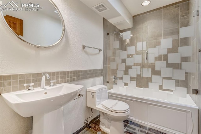 full bathroom with tile walls, bath / shower combo with glass door, sink, and toilet