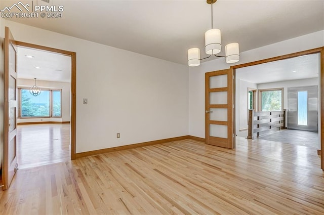 empty room with a notable chandelier and light wood-type flooring