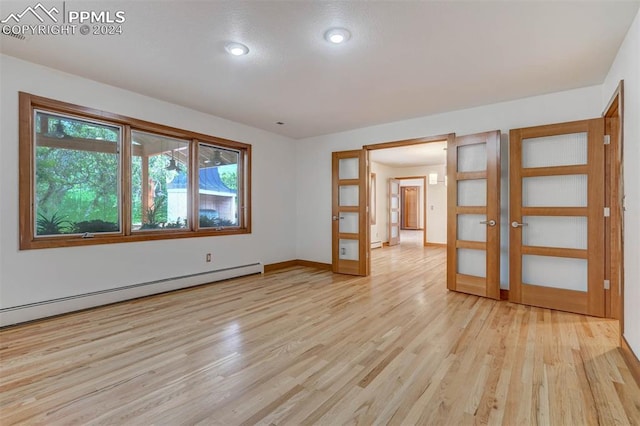 empty room featuring light wood-type flooring, french doors, and a baseboard radiator