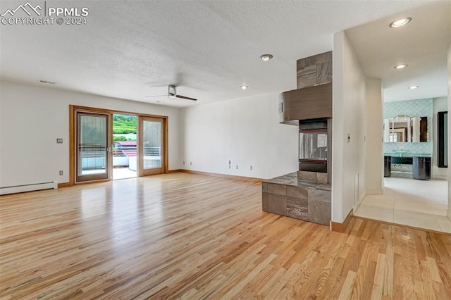 unfurnished living room with ceiling fan, a baseboard radiator, light hardwood / wood-style floors, and a textured ceiling