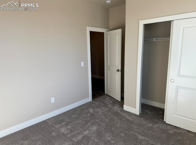 unfurnished bedroom with dark colored carpet, a closet, and baseboards