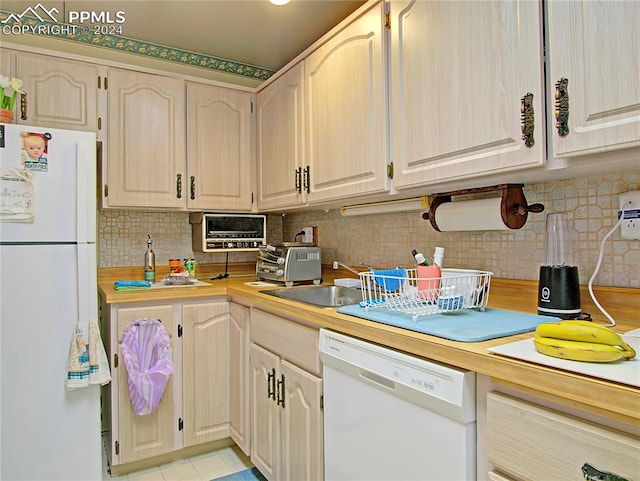 kitchen with white appliances, light tile patterned floors, light brown cabinetry, sink, and decorative backsplash