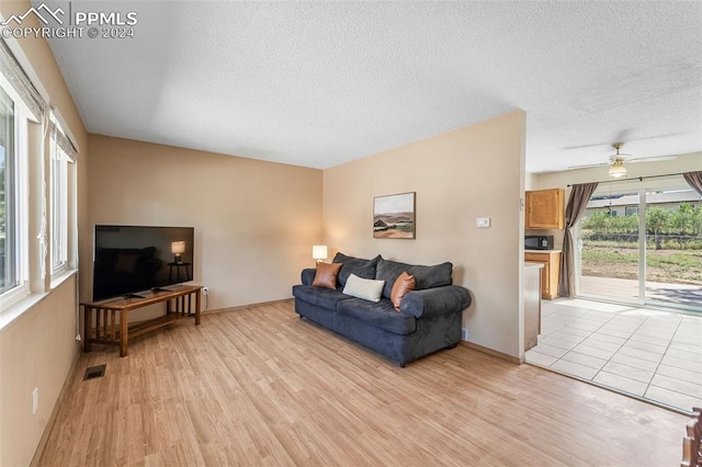 living room with ceiling fan, a textured ceiling, and light wood-type flooring