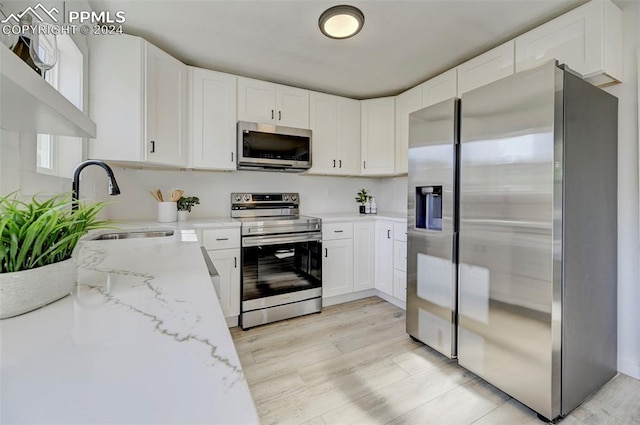 2459 E Willamette Ave, Colorado Springs, CO 80909 - kitchen with stainless steel appliances, light wood-style flooring, a sink, white cabinetry, and light stone counters
