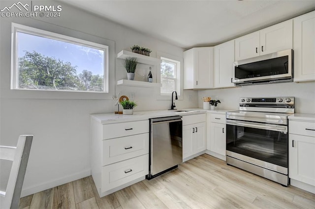 kitchen featuring light wood-type flooring, appliances with stainless steel finishes, light stone countertops, white cabinetry, and sink