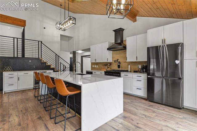 kitchen featuring stainless steel fridge, a center island with sink, high vaulted ceiling, decorative backsplash, and wall chimney range hood