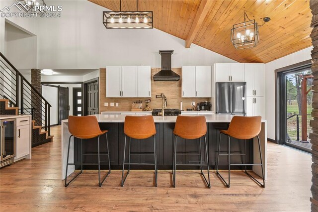 kitchen with stainless steel refrigerator, light hardwood / wood-style flooring, decorative backsplash, a breakfast bar area, and wall chimney range hood