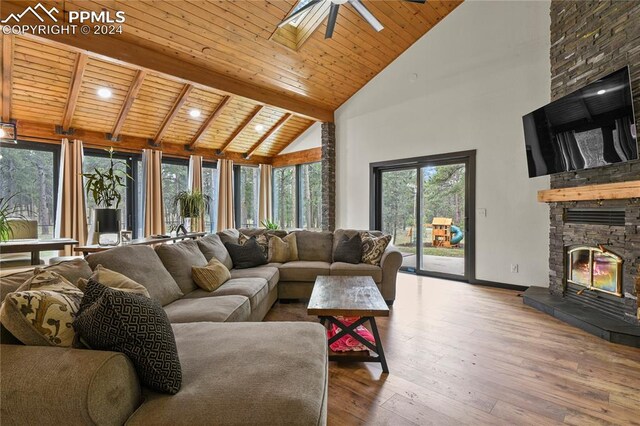 living room featuring high vaulted ceiling, light hardwood / wood-style flooring, ceiling fan, a stone fireplace, and wood ceiling